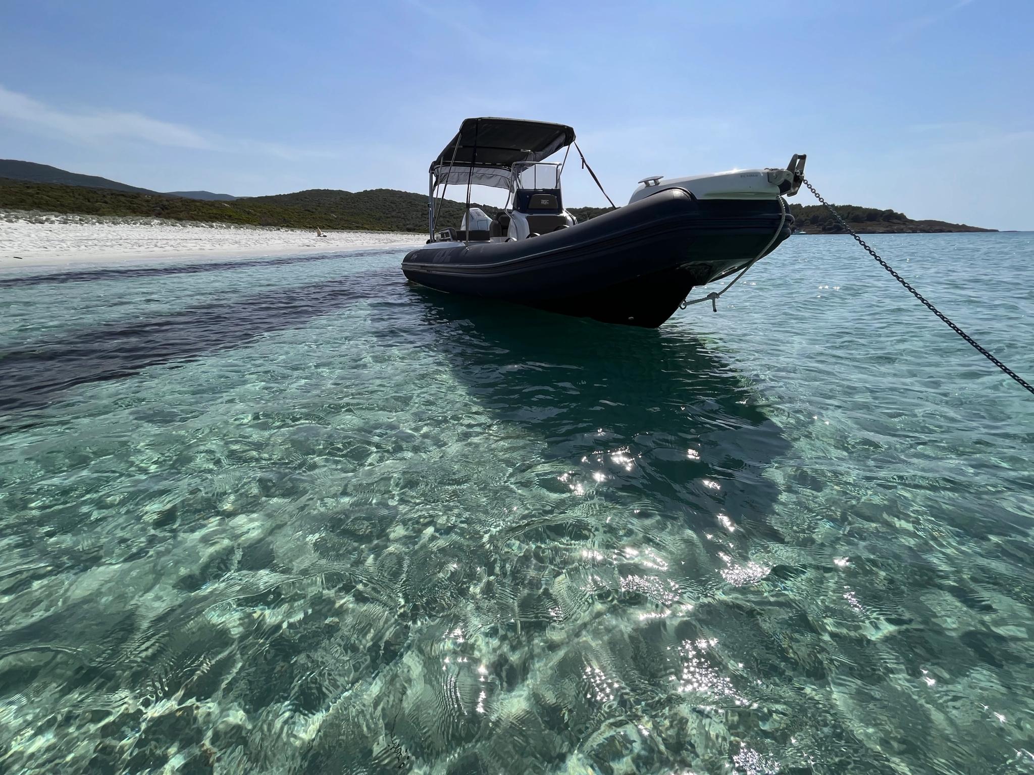 Bateau noir ancré en eaux turquoise pour location à Île-Rousse en Balagne